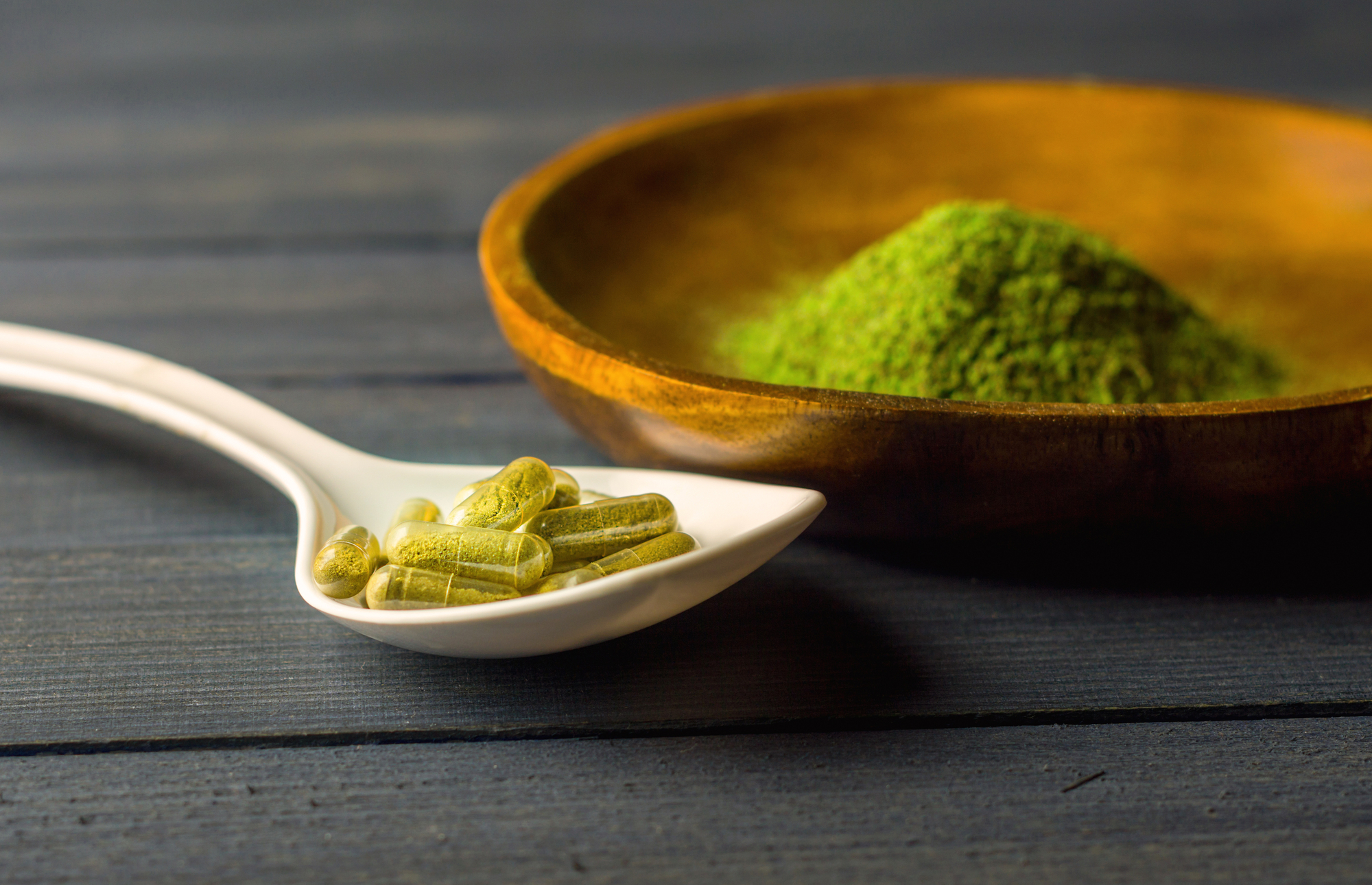 Mitragynina speciosa or Kratom powder in wooden bowl and Kratom capsules in ceramic spoon on table