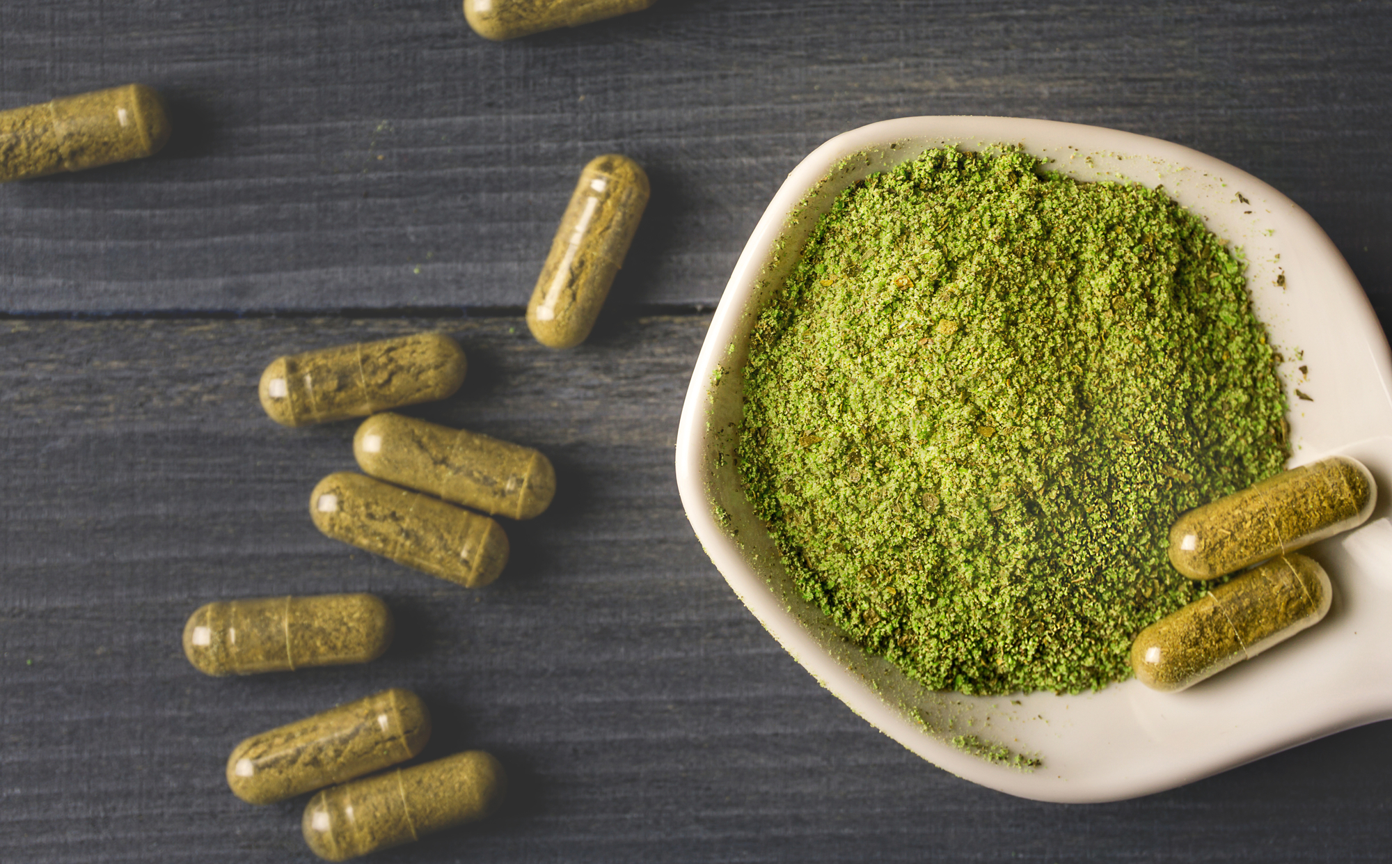 Top view of Kratom powder in ceramic spoon and Kratom capsules on wooden table